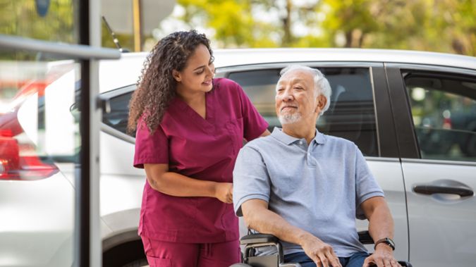 A man in a wheelchair is pushed by his caregiver. 