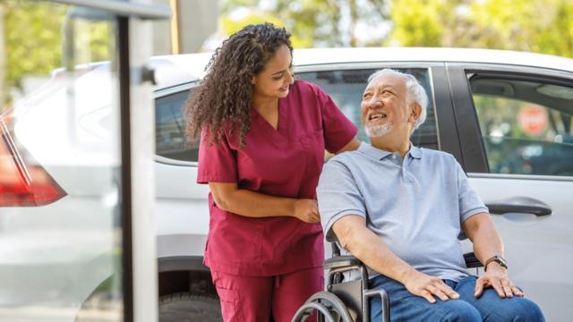 A man in a wheelchair smiles at his caregiver as she pushes him.