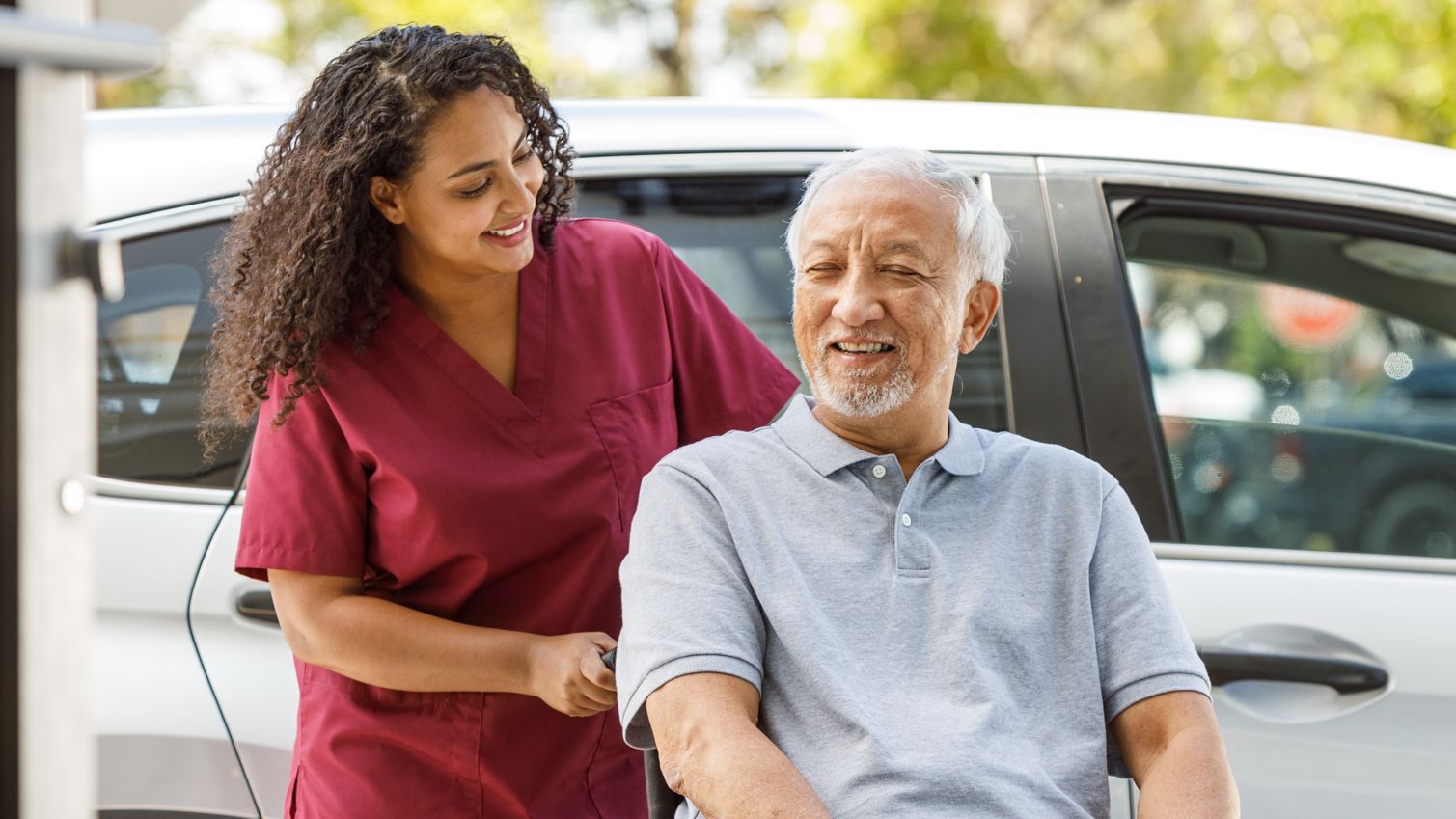 A man in a wheelchair smiles at his caregiver as she pushes him.