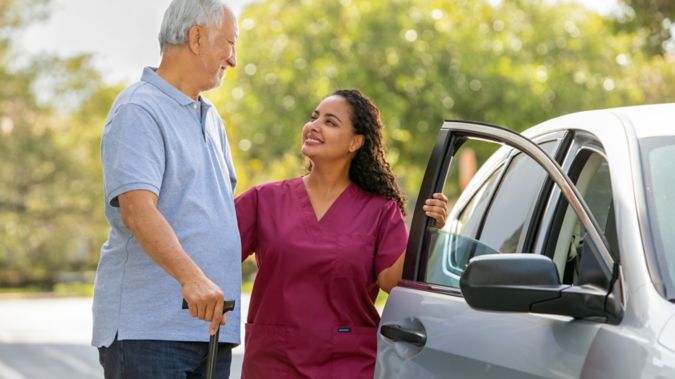 A man is helped into a car by a caregiver.