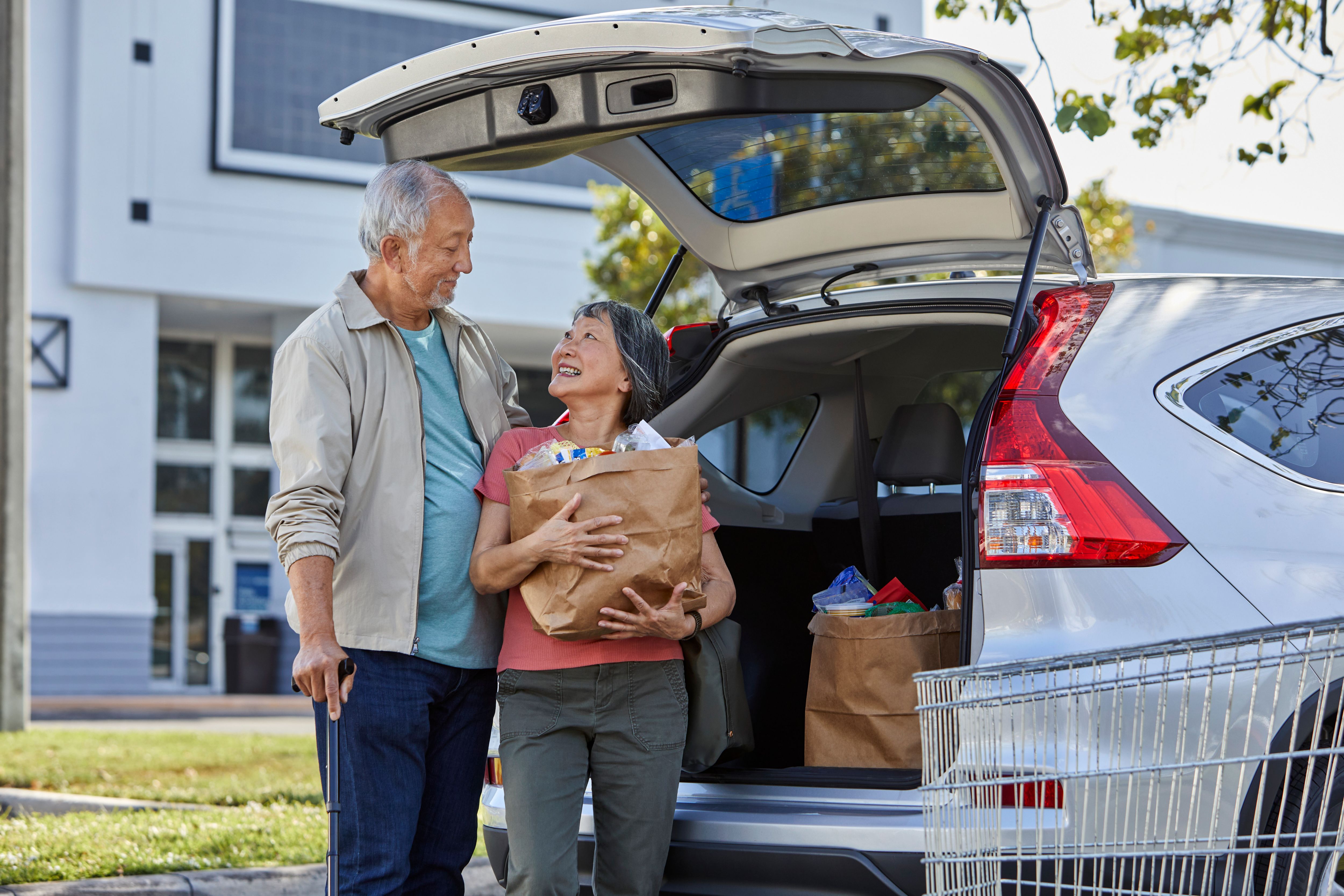 Seniors loading groceries into trunk of SUV.