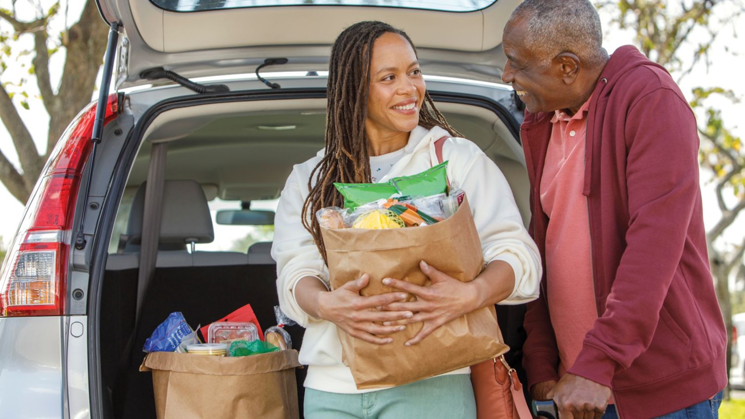 A man gets help from his daughter to carry in groceries from his trunk. 