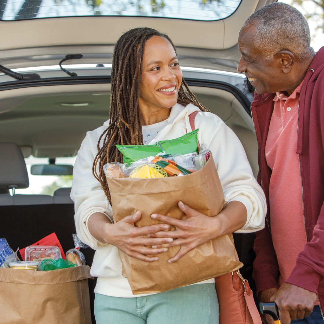 A woman helps her father carry in groceries from his car. 