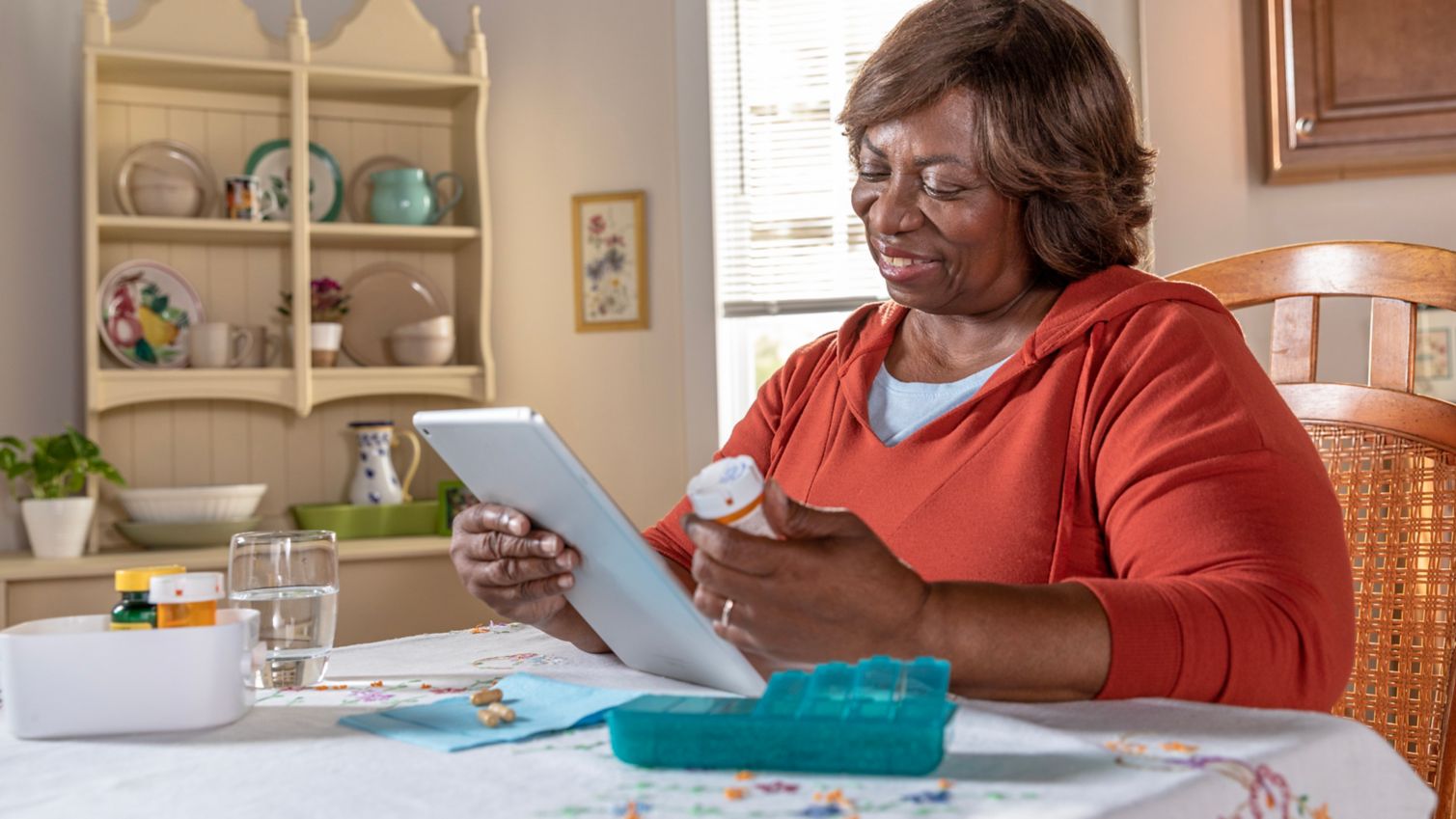 Woman reading tablet and prescription bottle at table.