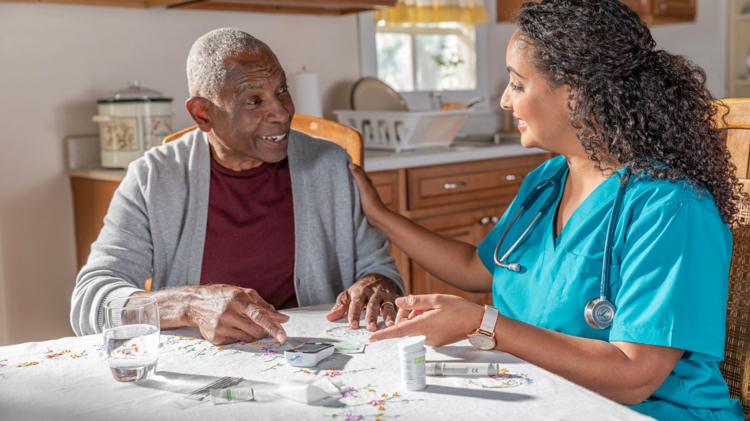 Senior man and nurse sitting at kitchen table having wellness visit in his home.