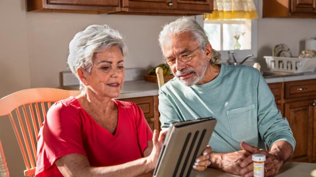 Man and woman sitting at a table and looking at tablet.