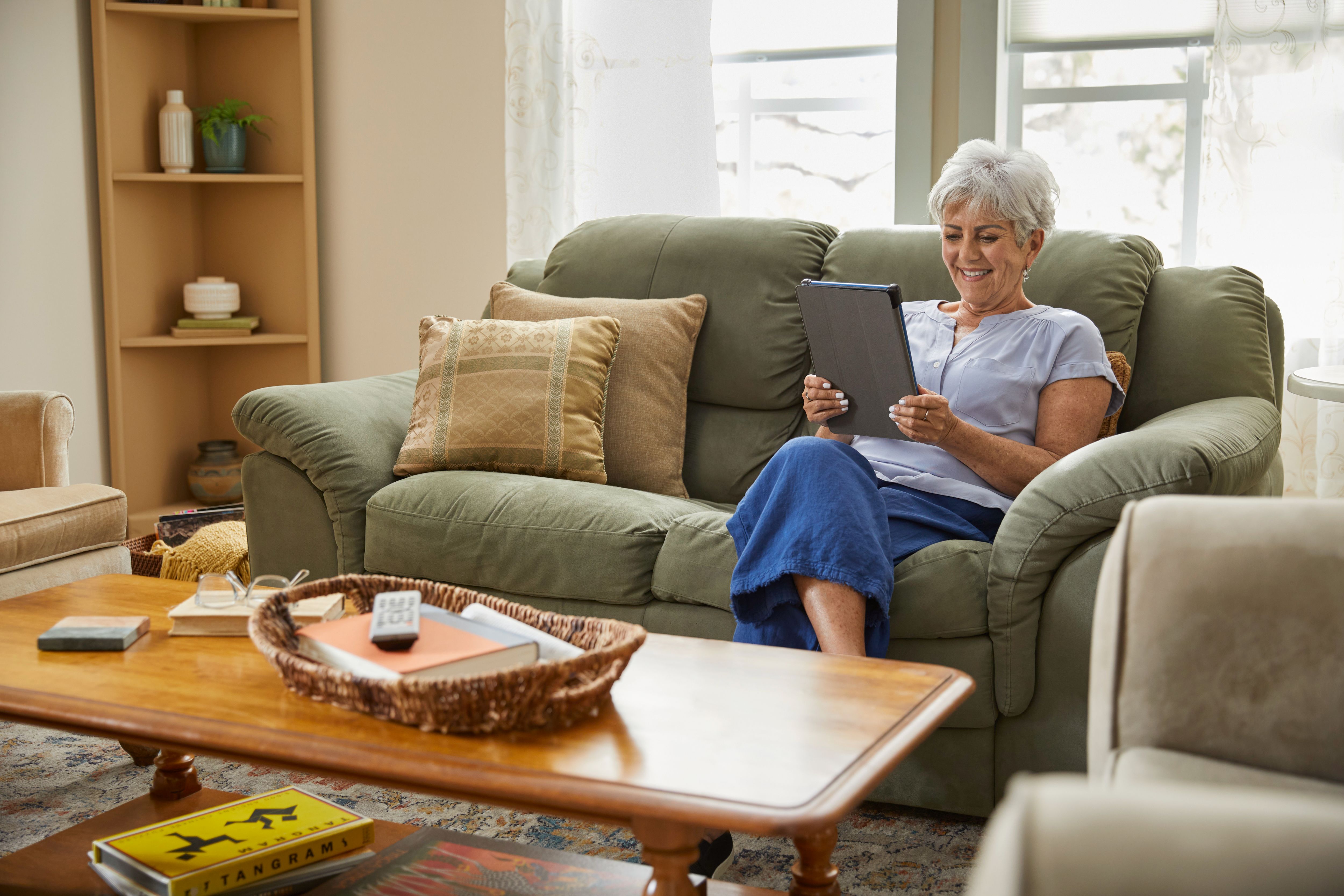 Senior woman sitting on couch smiling having telehealth visit on tablet