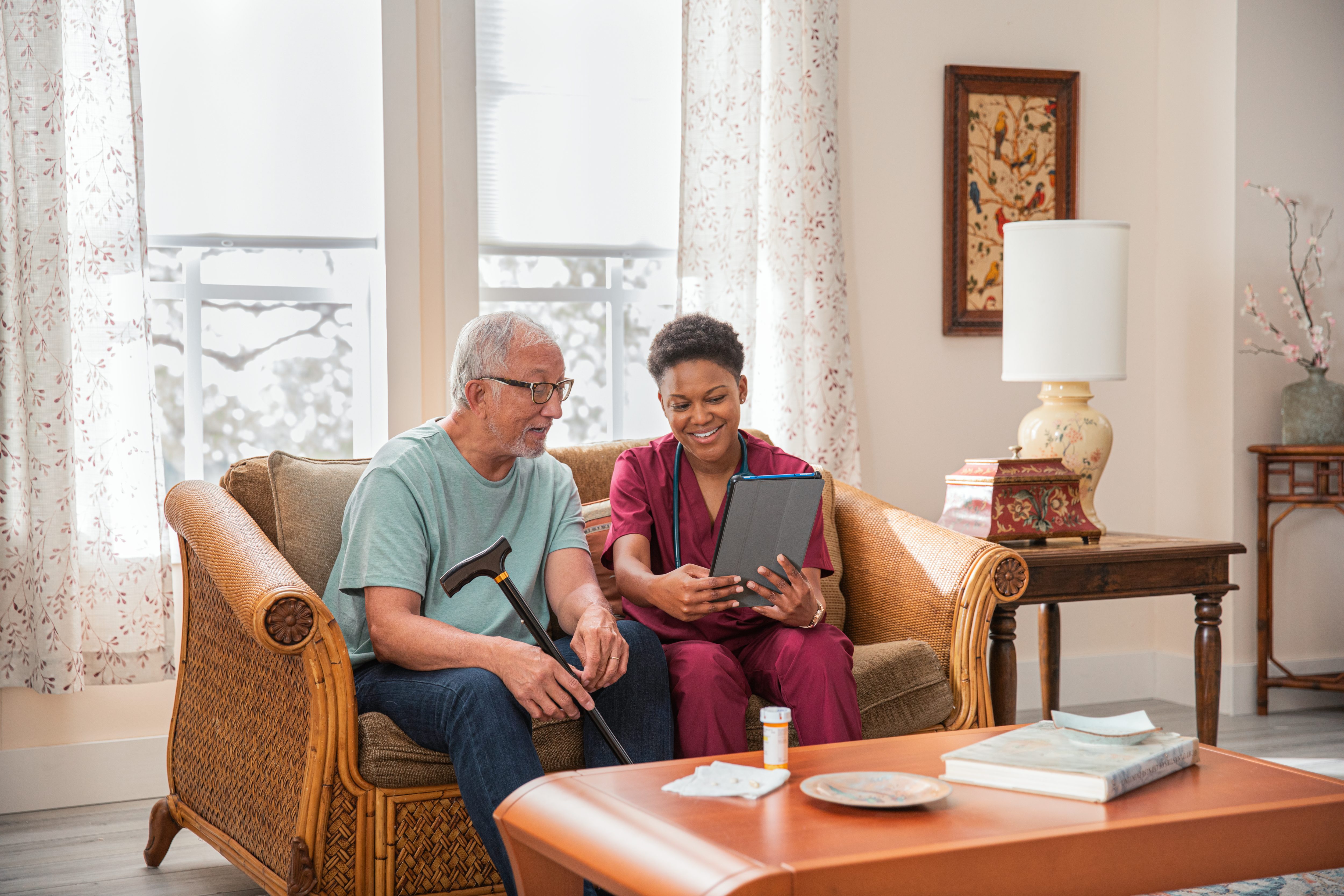 Senior man sits on couch with nurse caregiver reviewing medication