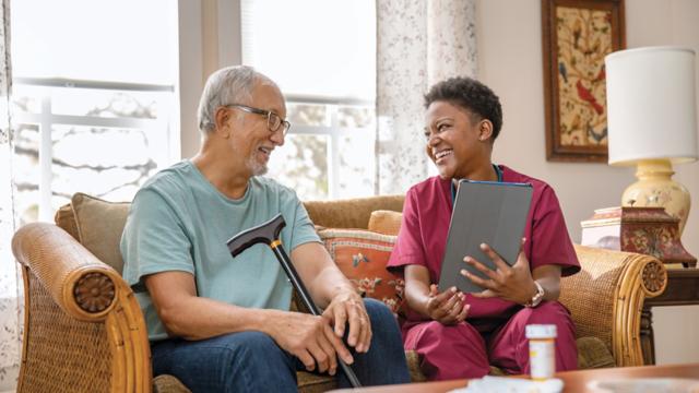 A man laughs while meeting with his caregiver in his living room. 