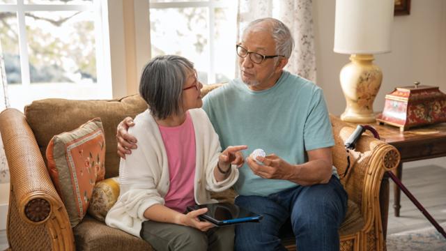 A couple sits close on their sofa while reviewing a prescription label and a tablet.