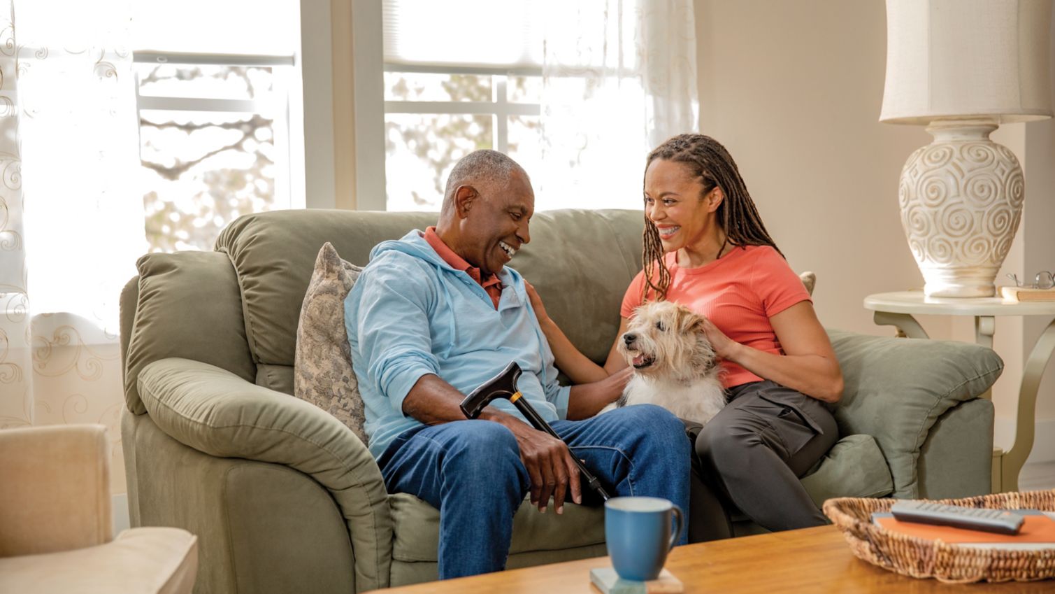 Man and his adult daughter sit on his sofa with his dog.