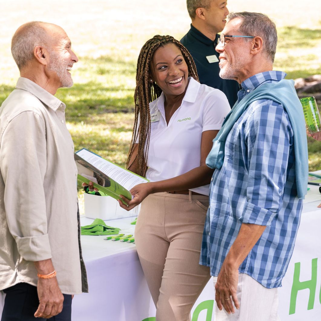 2 older men talk to female Humana employee.