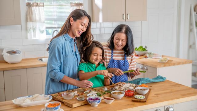 A woman prepares a meal with her daughter and grandchild. 