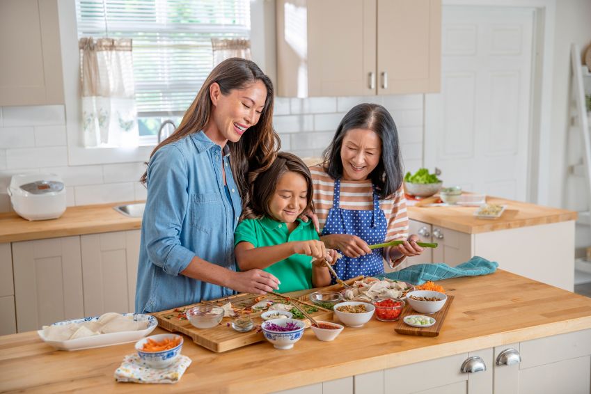 A woman prepares a meal with her daughter and grandchild. 