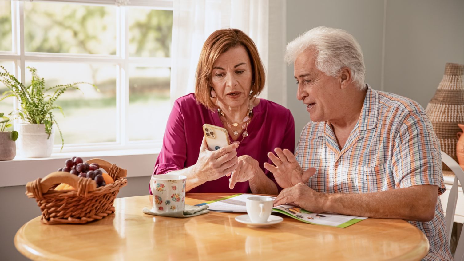 Senior couple sitting together at table reviewing brochure and phone