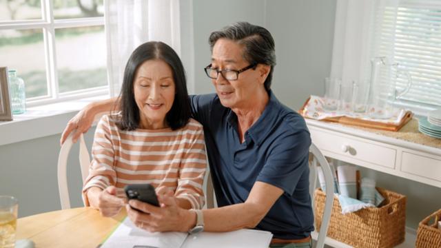 Older couple looks at phone and brochure.