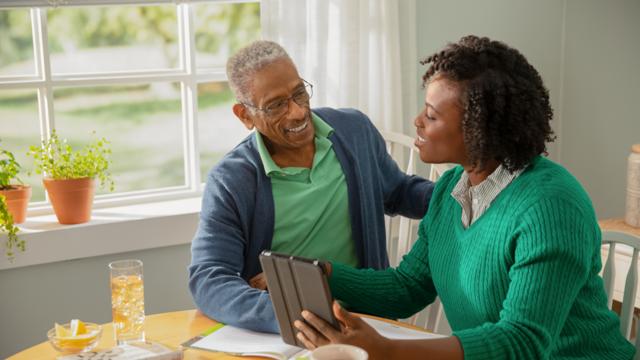 A man gets help from his adult daughter to use a tablet for a video visit. 