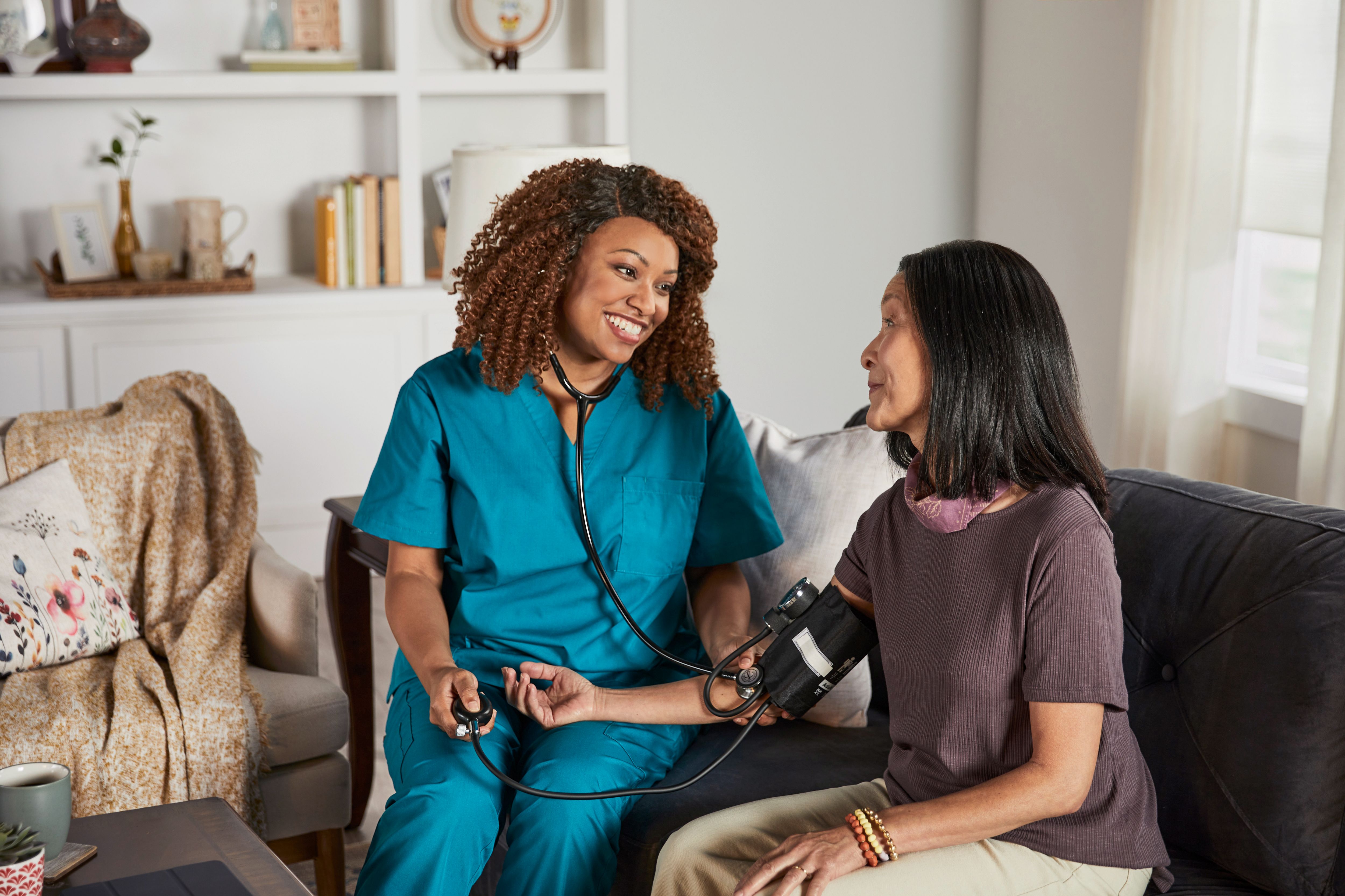 A provider smiles while taking the blood pressure reading of a patient in their home. 