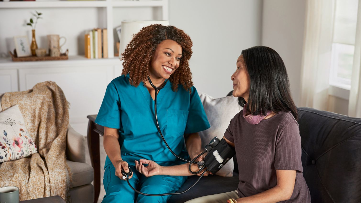 A woman has her blood pressure taken in her home by a caregiver. 
