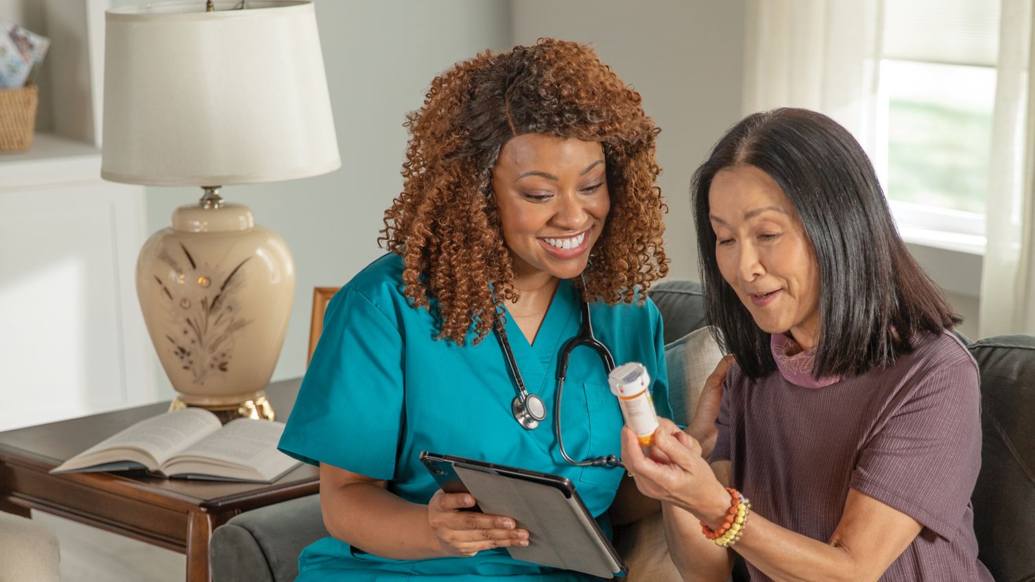 A woman sits in her living room with her caregiver and reviews a prescription label. 