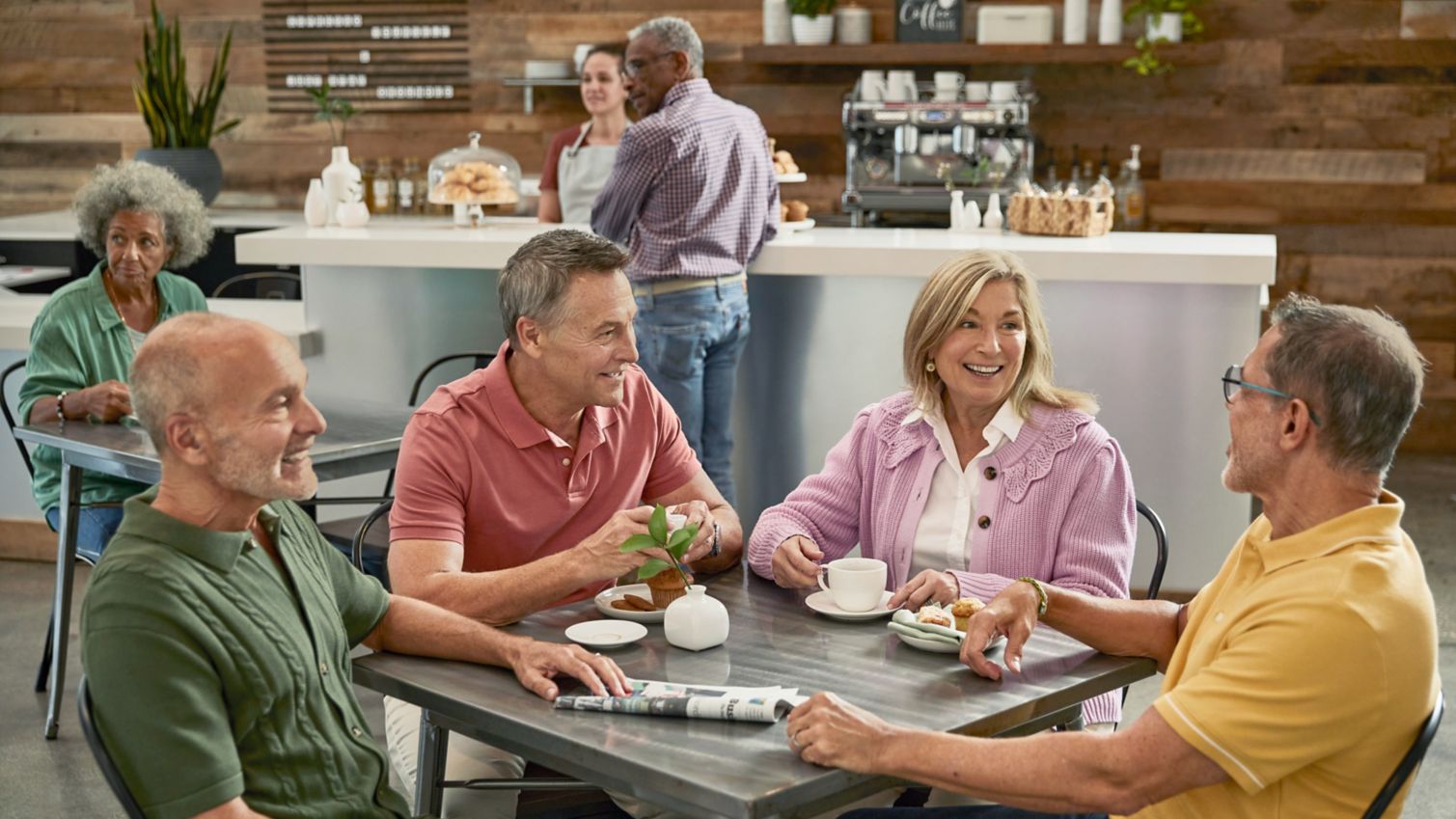 A group of seniors smile as they chat in a coffee shop. 