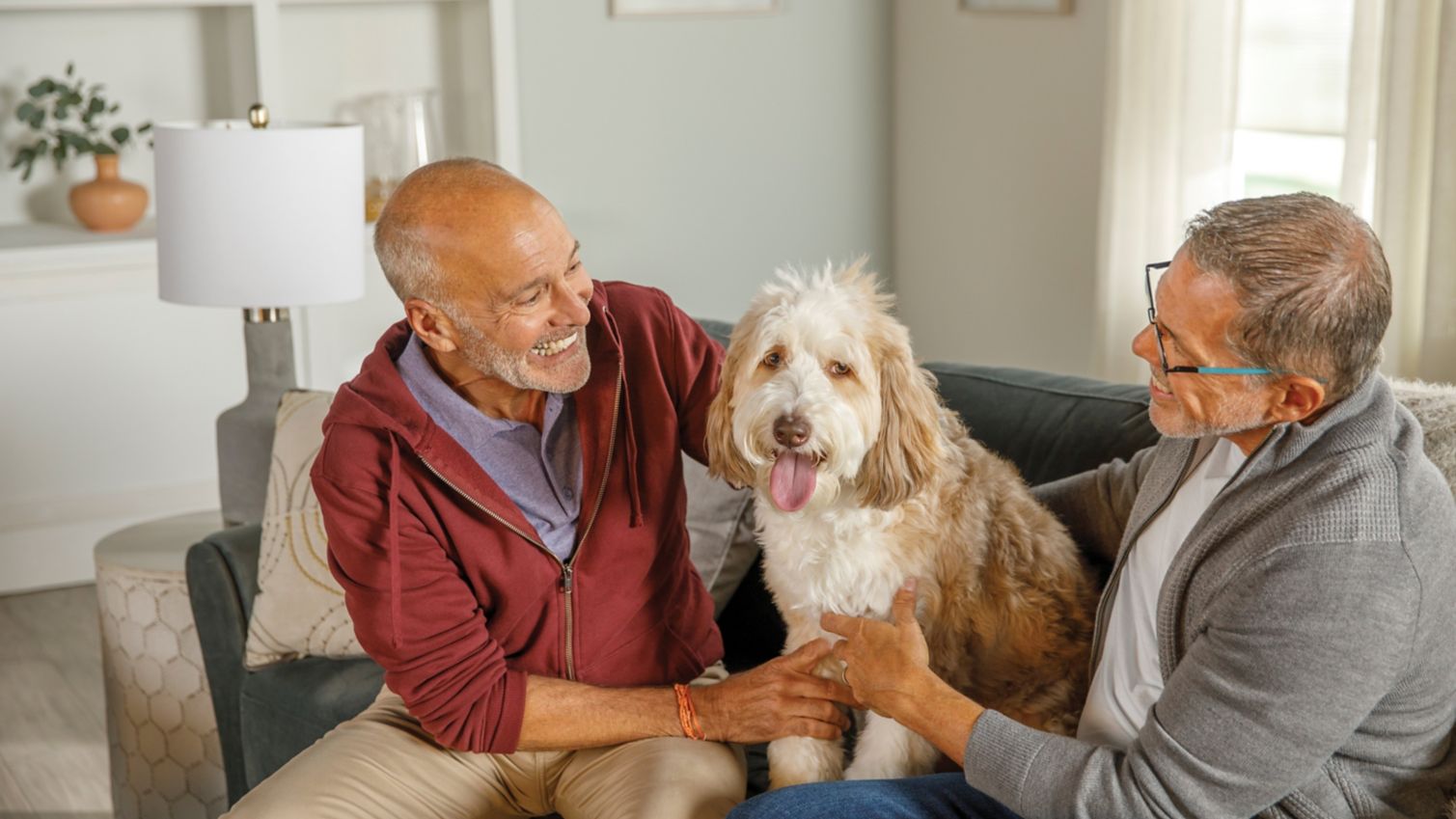 A couple laughs while snuggling their dog on the couch. 