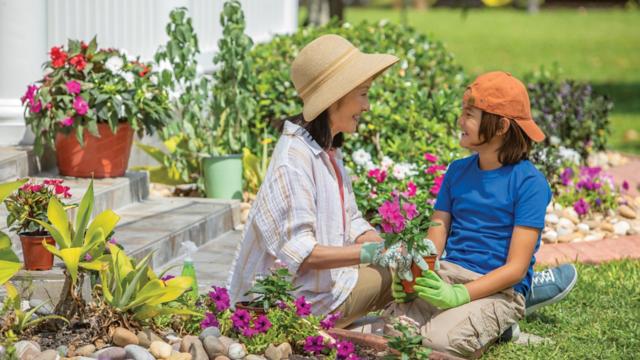 A woman and her grandson plant flowers in her garden beds.