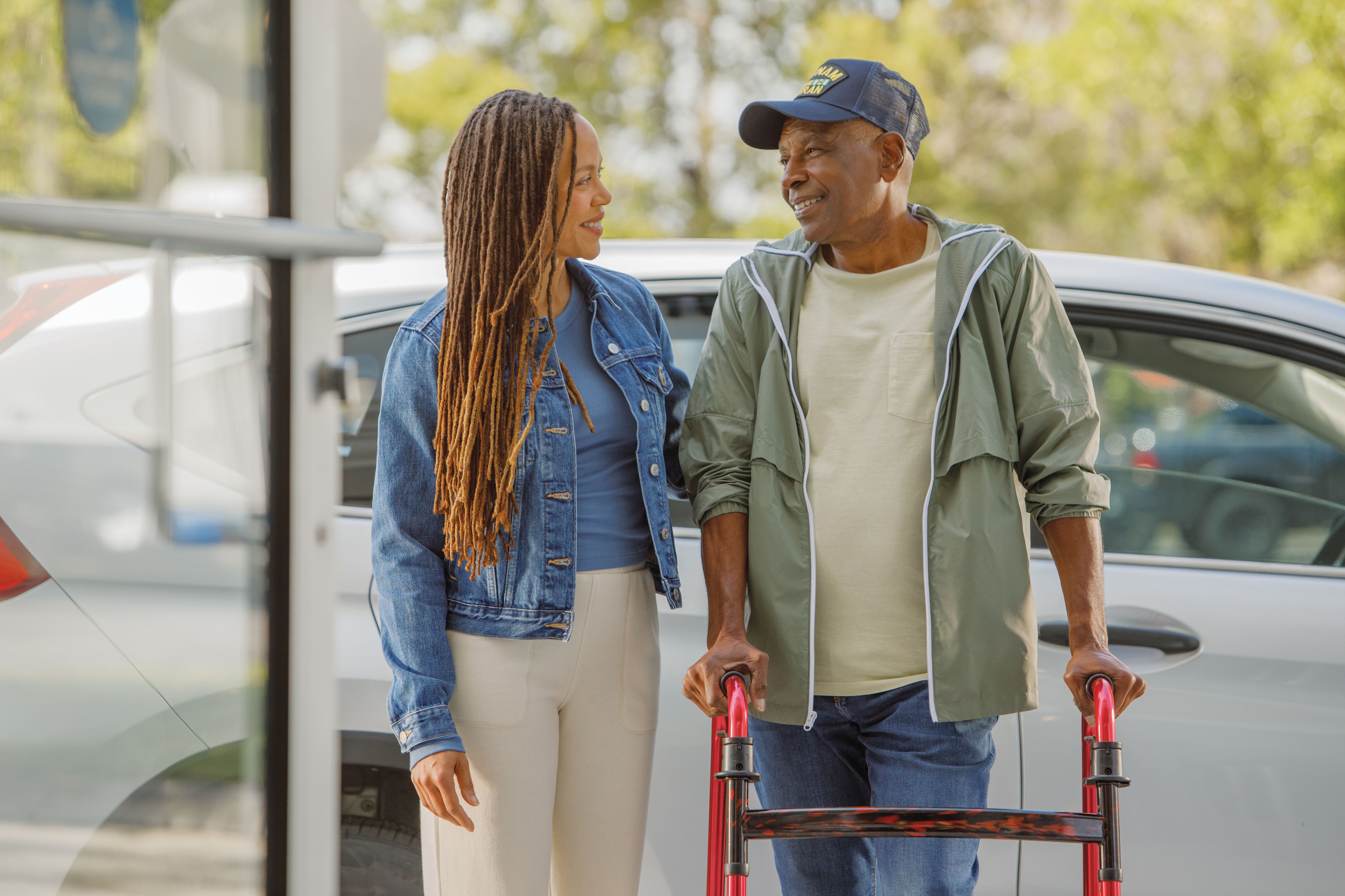 Senior man using walker receives assistance from adult daughter getting from car to entrance of doctor office