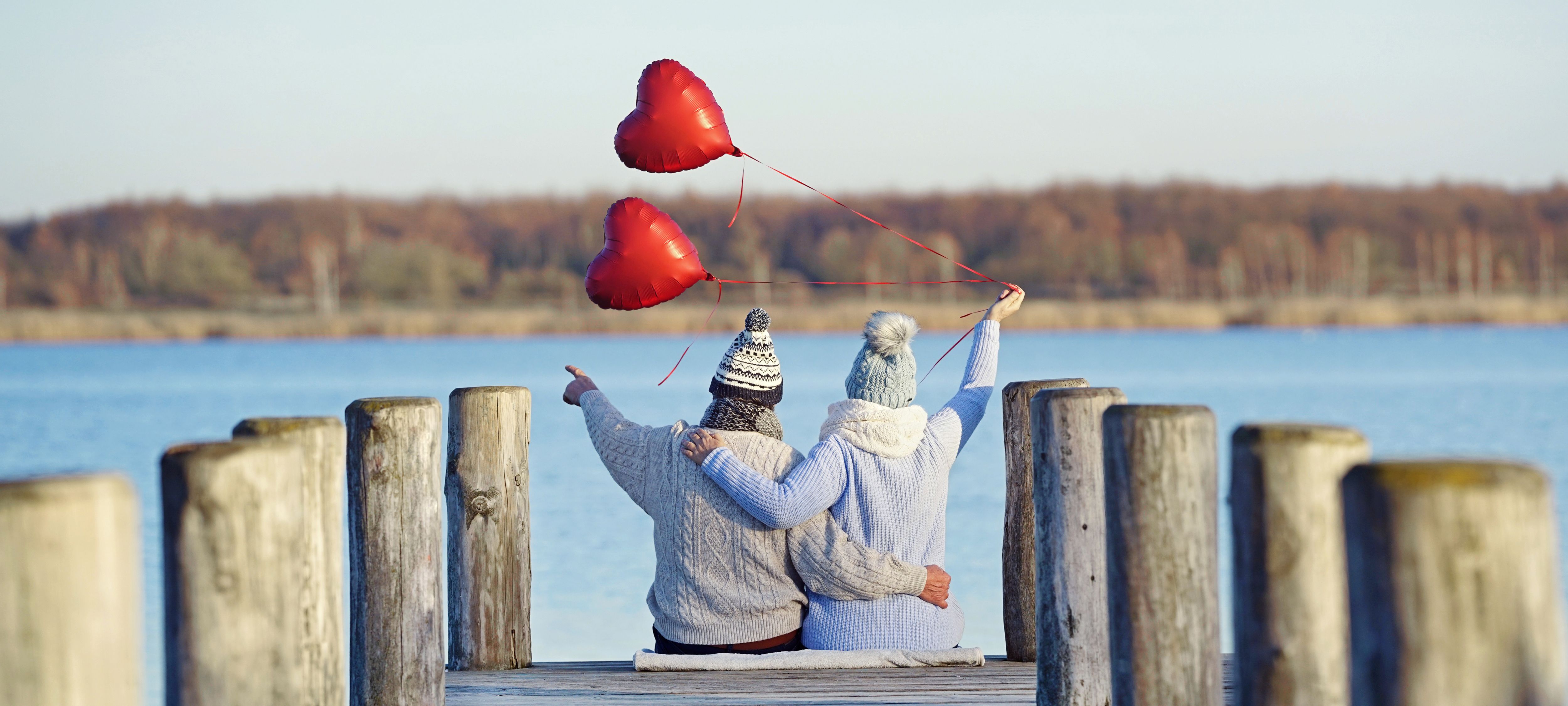 elderly couple in love sitting on wooden jetty - romantic date at the beach in winter