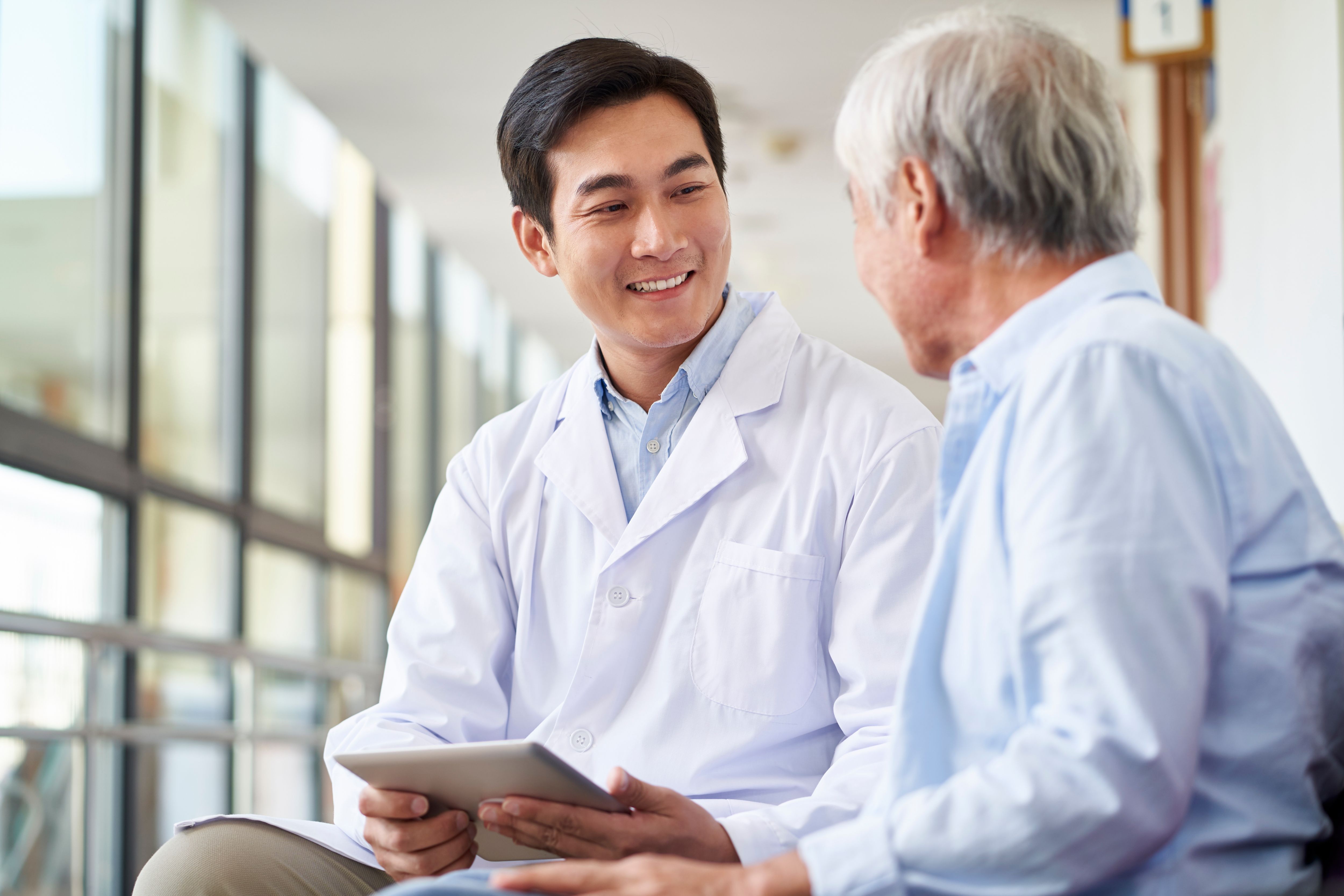 friendly smiling young asian doctor talking and explaining test result to elderly patient in hospital