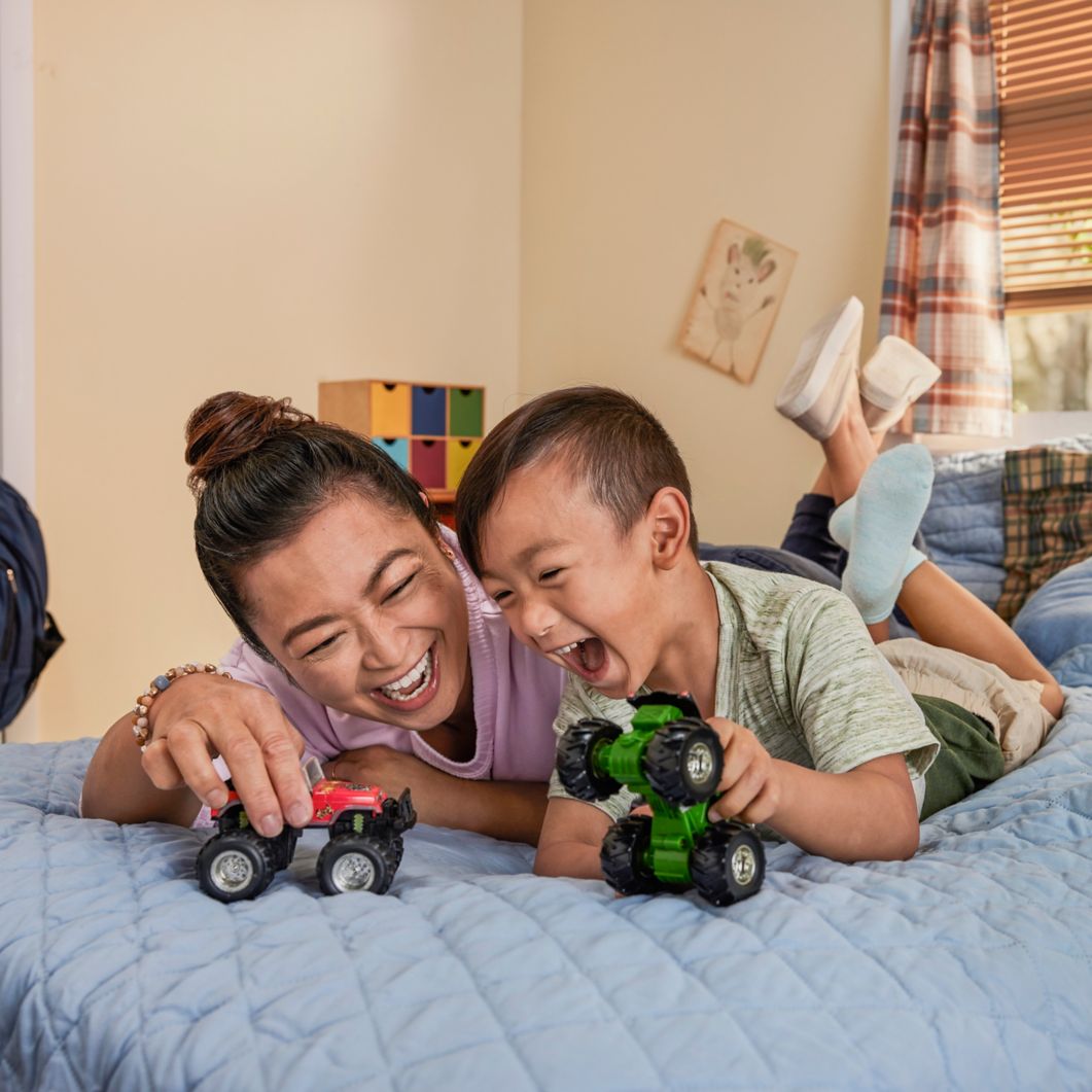 An adult and child play with toys on a bed