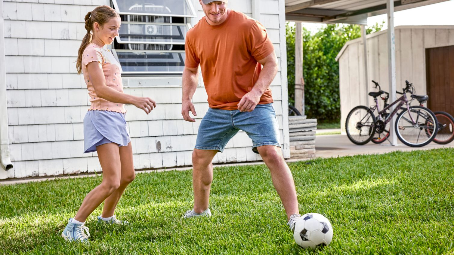 Dad and teen playing with soccer ball in yard