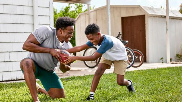 adult and child playing with football in yard