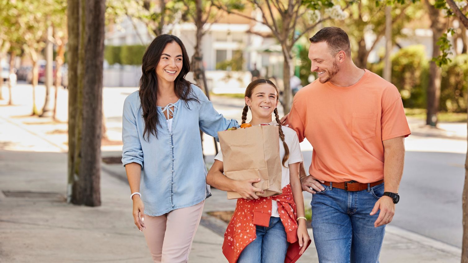 Two adults walking with a child carrying a bag of groceries