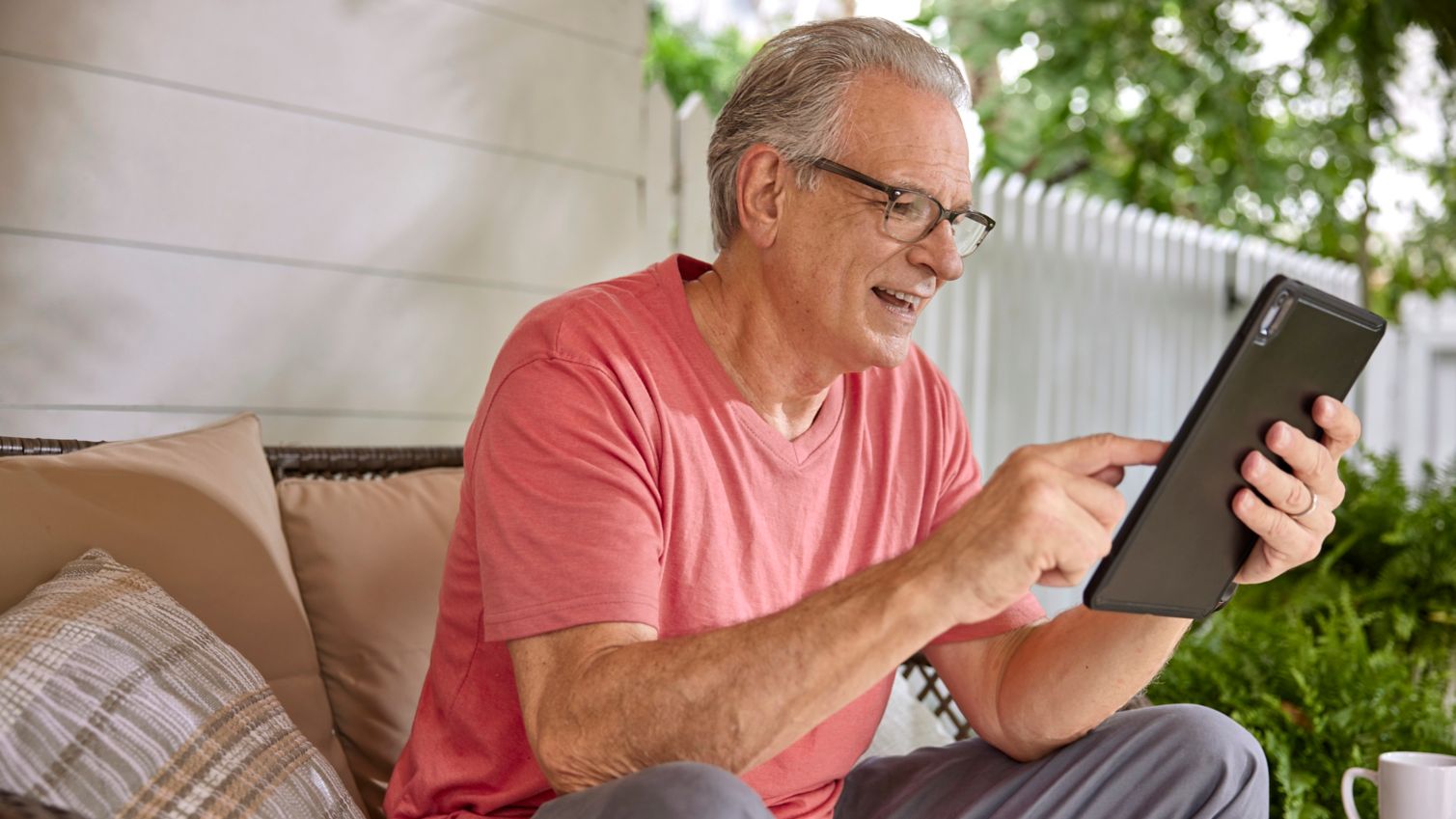 Senior sitting outdoors scrolling on a tablet computer.