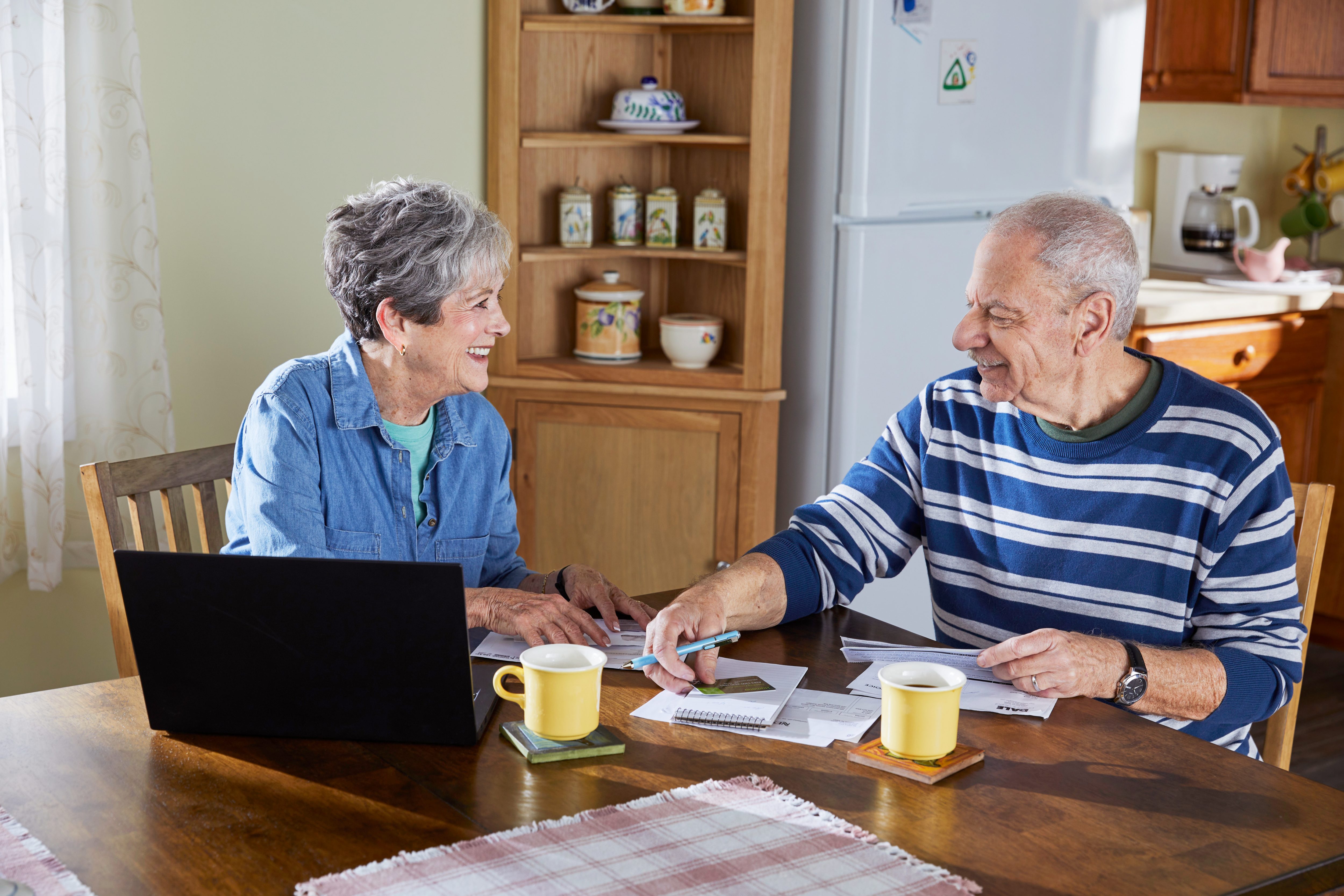Couple paying bills at kitchen table with laptop