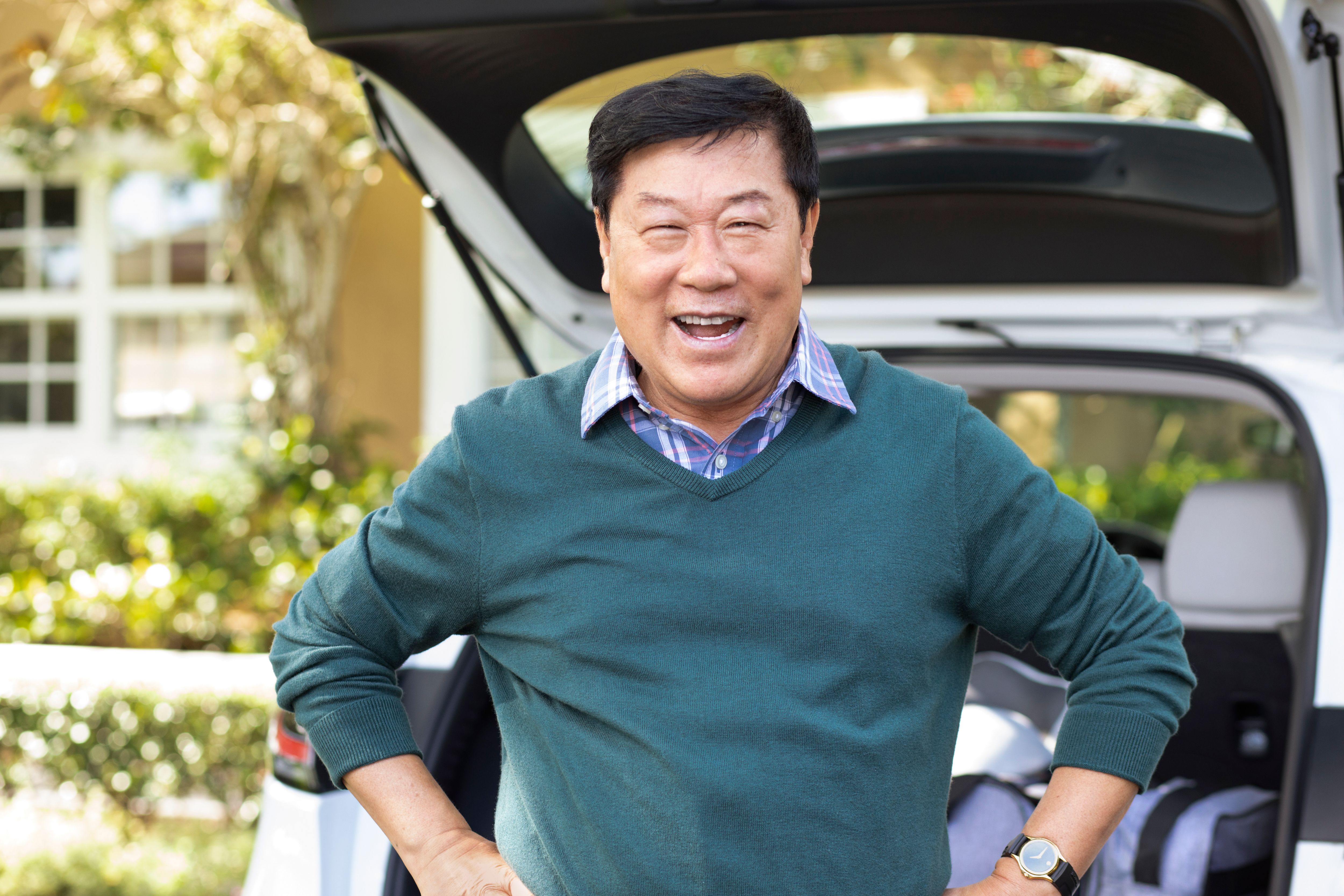 Portrait of senior getting ready for a trip, standing next to car with luggage.