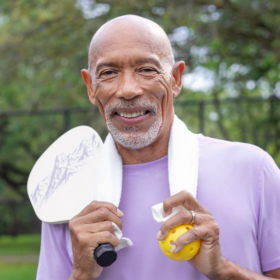 Man smiling while holding pickleball paddle and ball.
