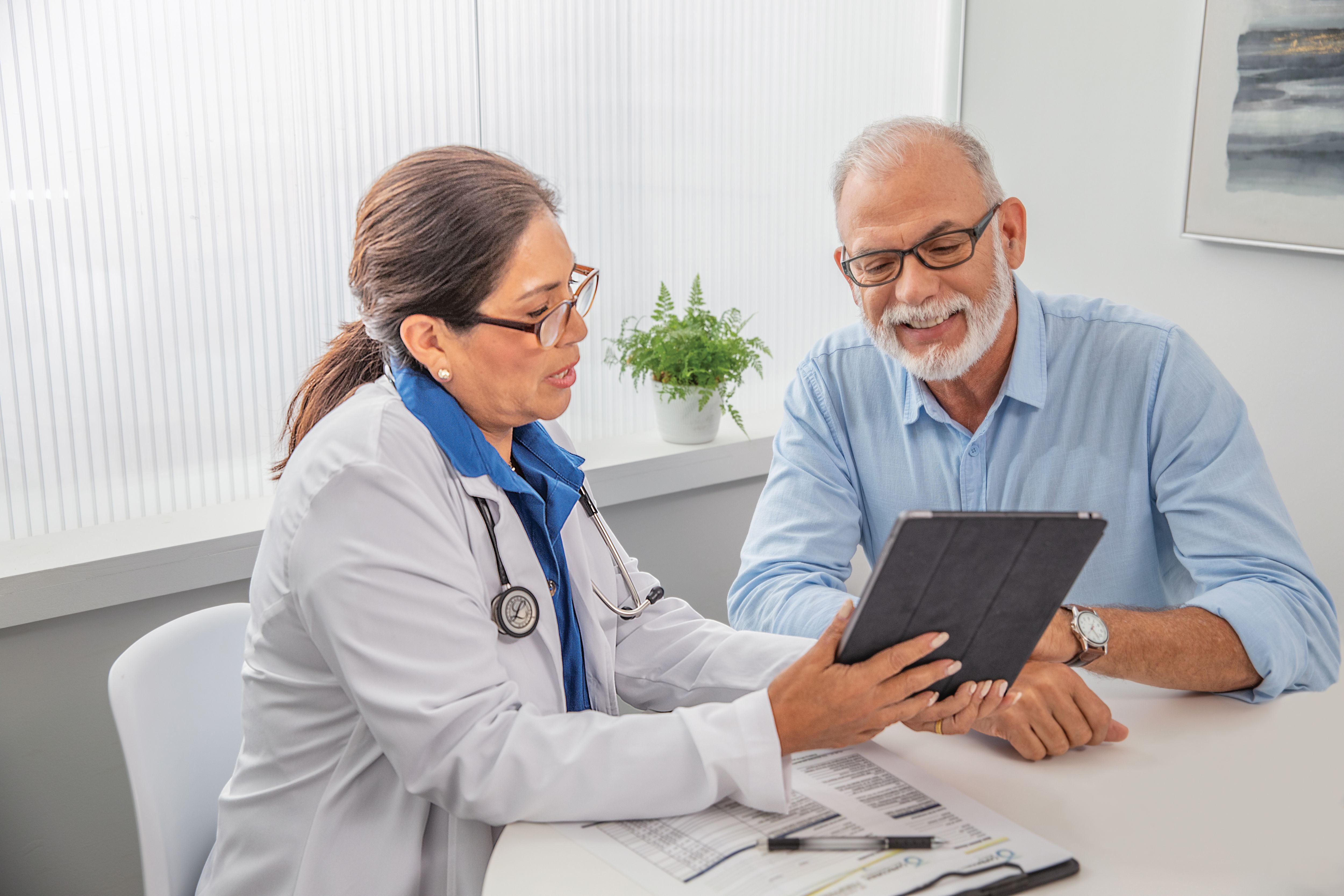 Senior man meeting with doctor both are looking at tablet together.