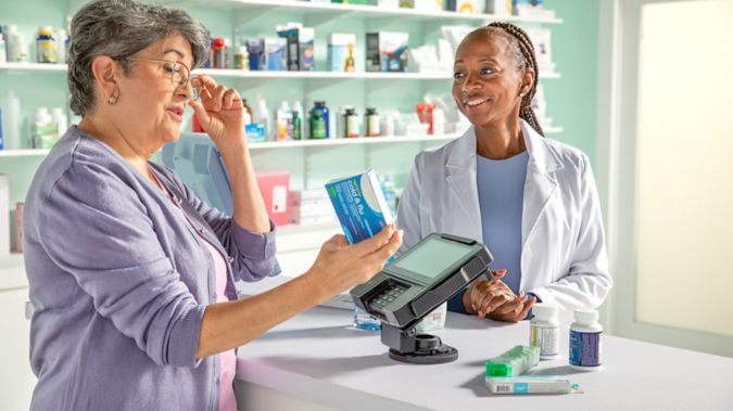 Senior woman reading meciation package at pharmacy counter with pharmacist