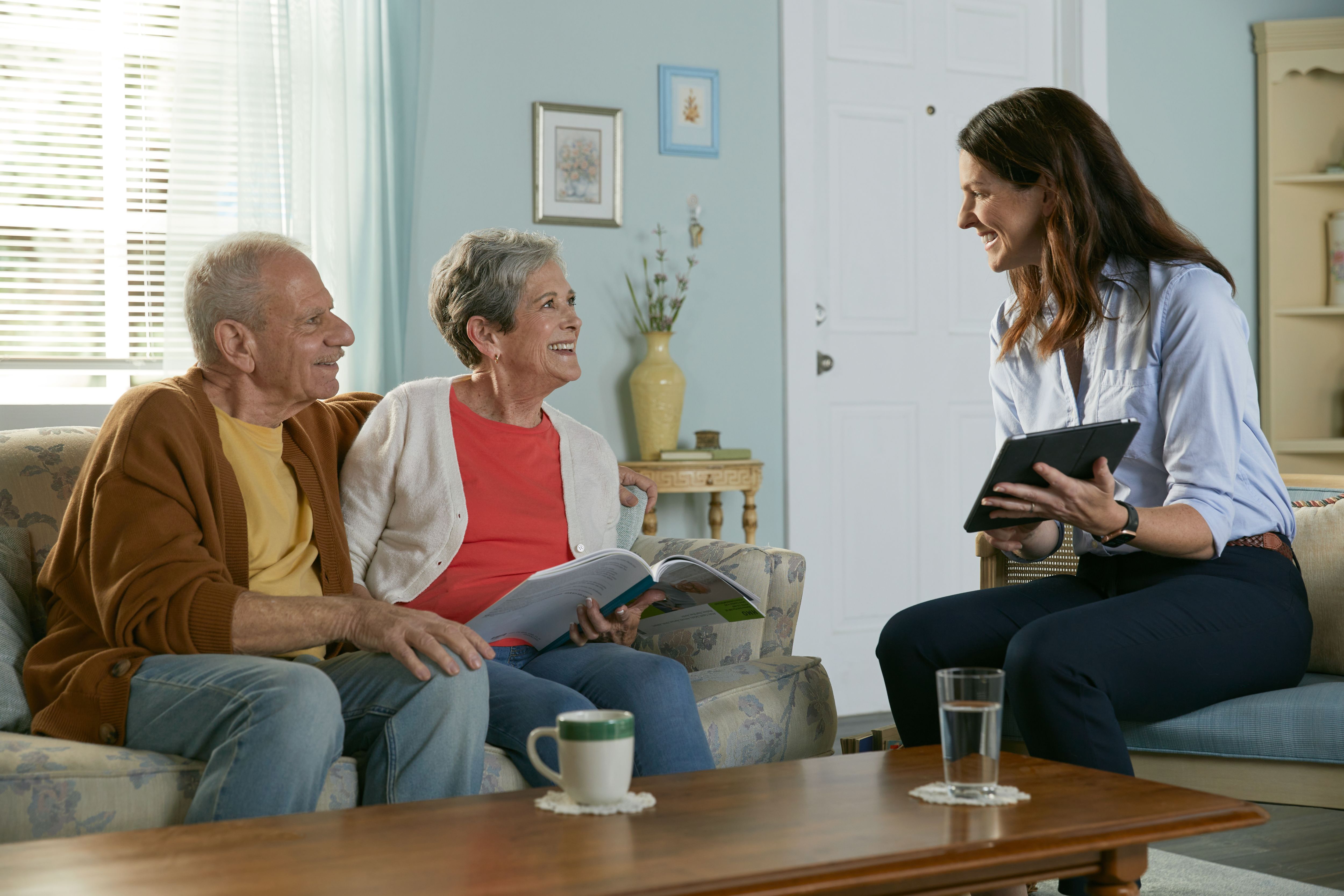 Agent reviewing plan options on tablet with senior couple in living room.