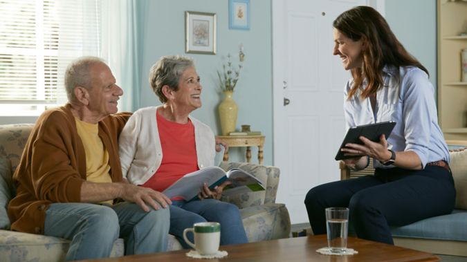 Agent reviewing plan options on tablet with senior couple in living room.