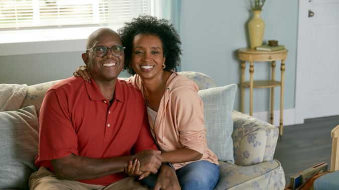 A retired man sits on the couch with his daughter