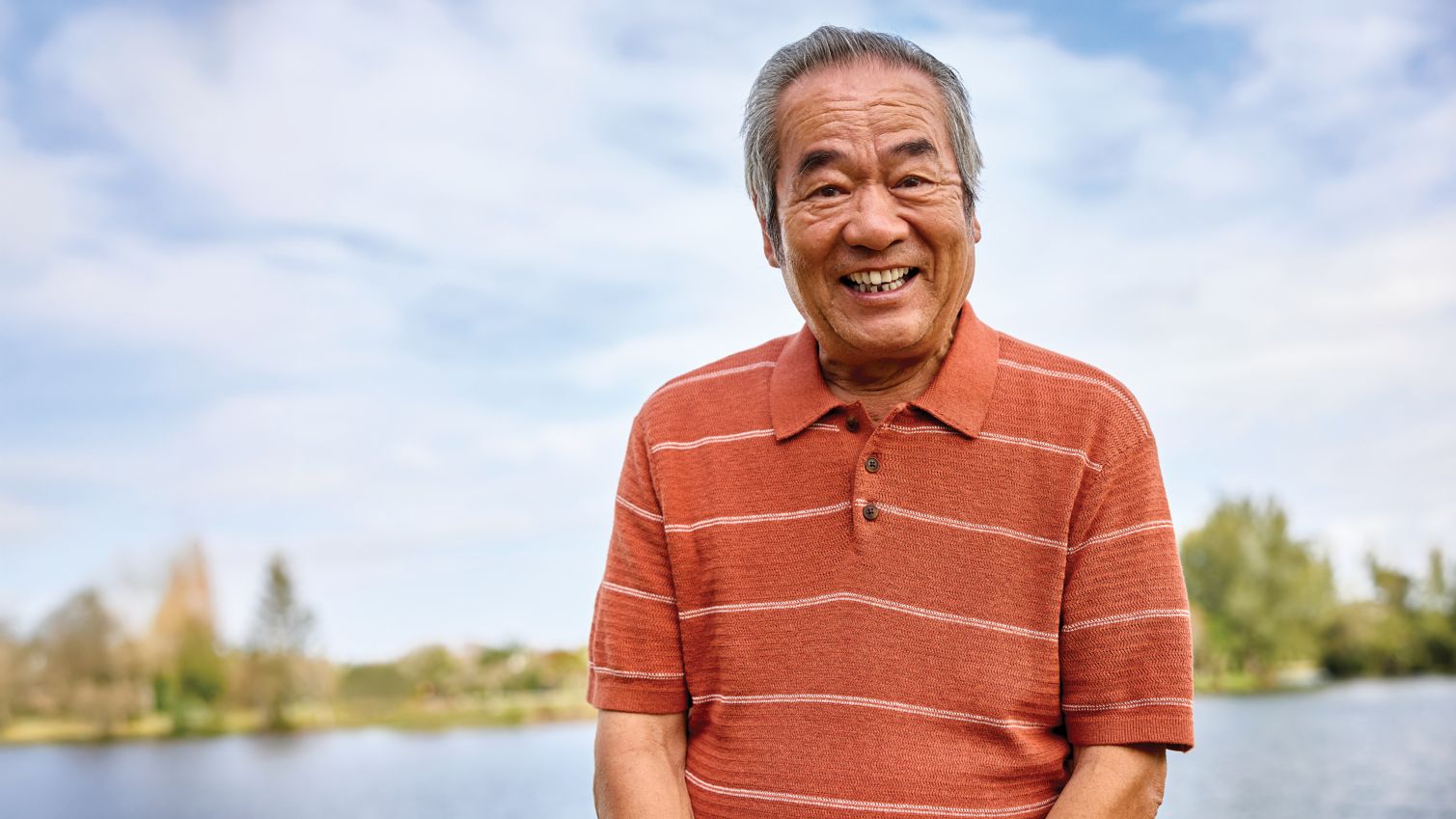 Man smiling and standing in front of a lake.