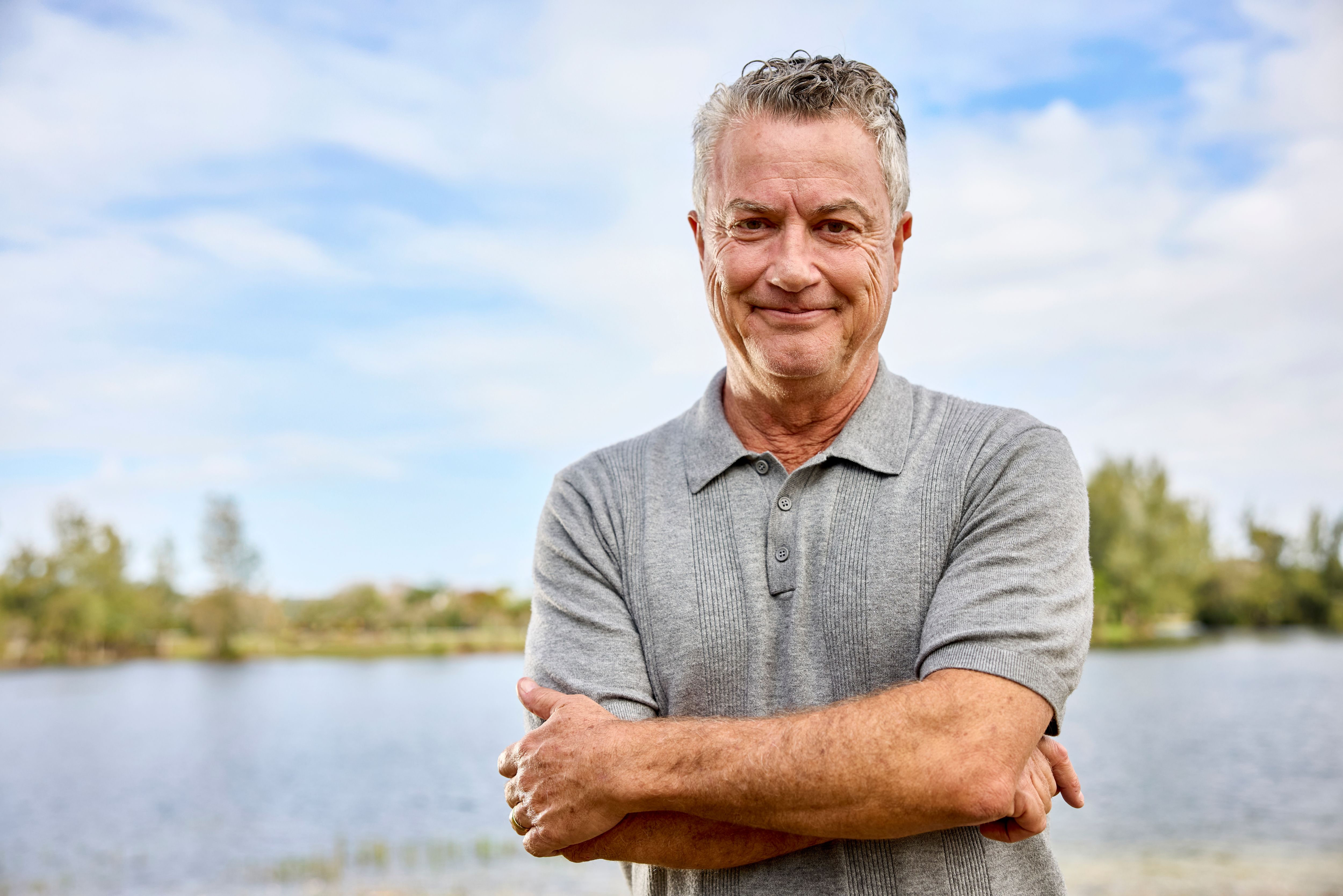 Man smiling and standing by a lake. 