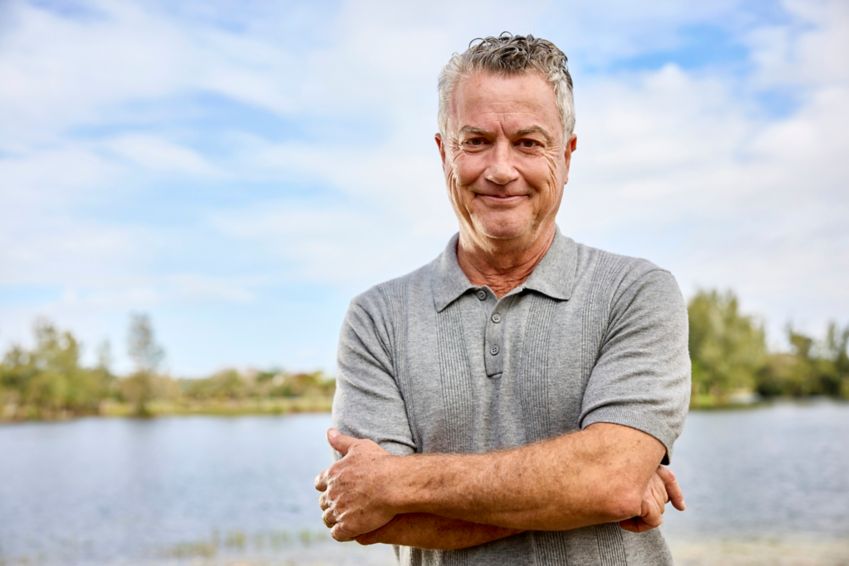 Man smiling and standing by a lake. 