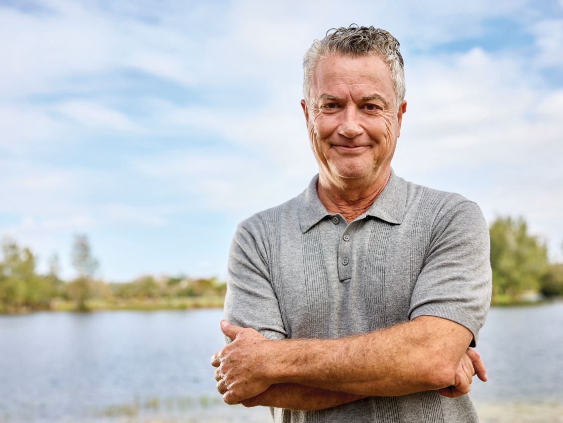 Man smiling and standing by a lake.