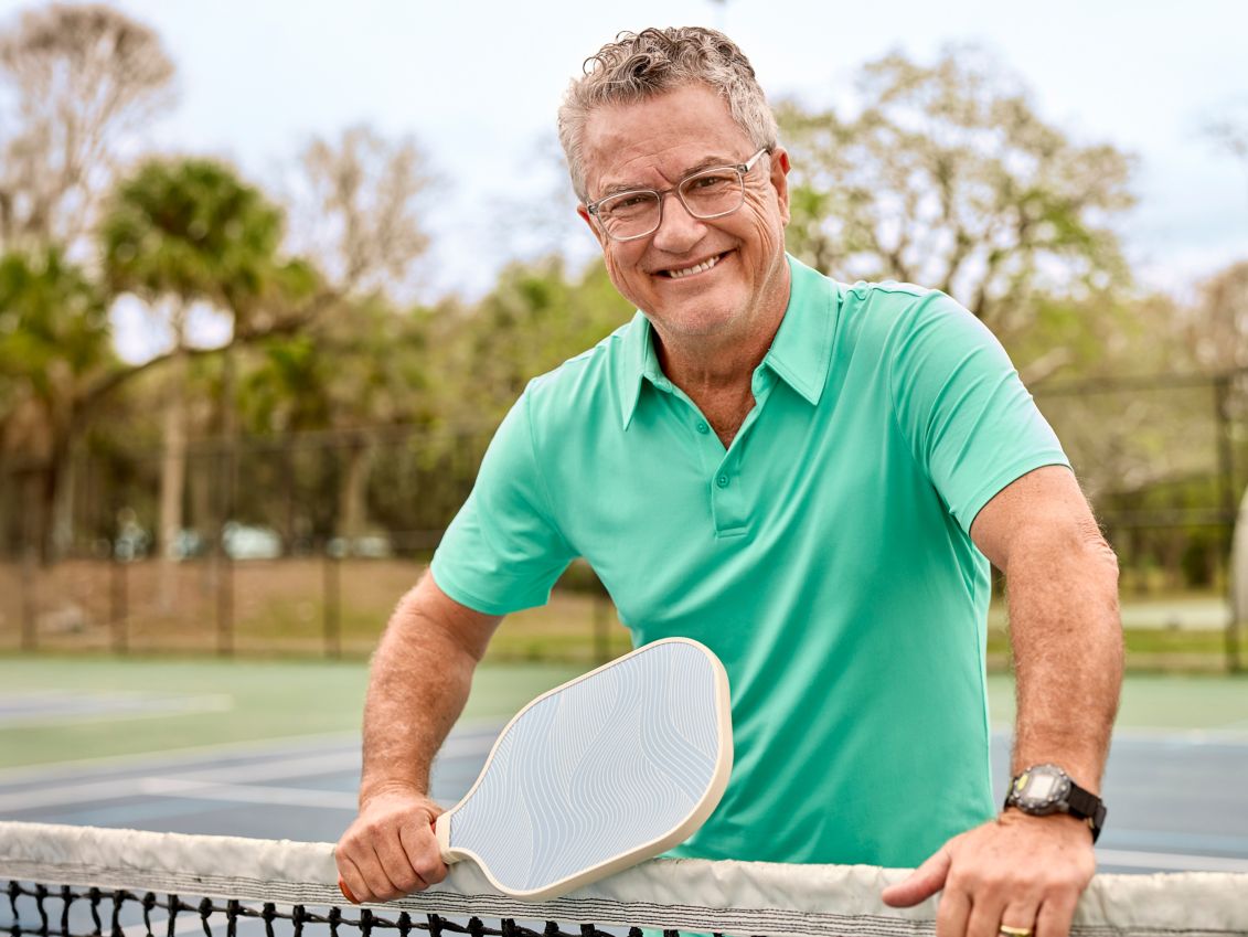 Man smiling at a pickle ball court.