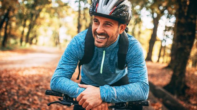 Smiling man riding bicycle on tree-lined path.
