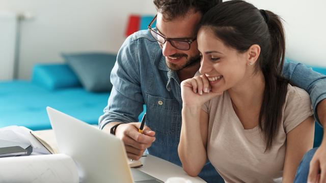 Couple smiling while working together on laptop.